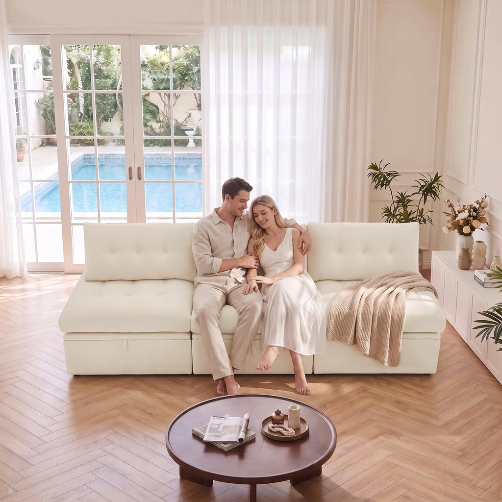 Side level view of a couple sitting on a Korser beige 3-seater straight modular storage sofa with backrests.