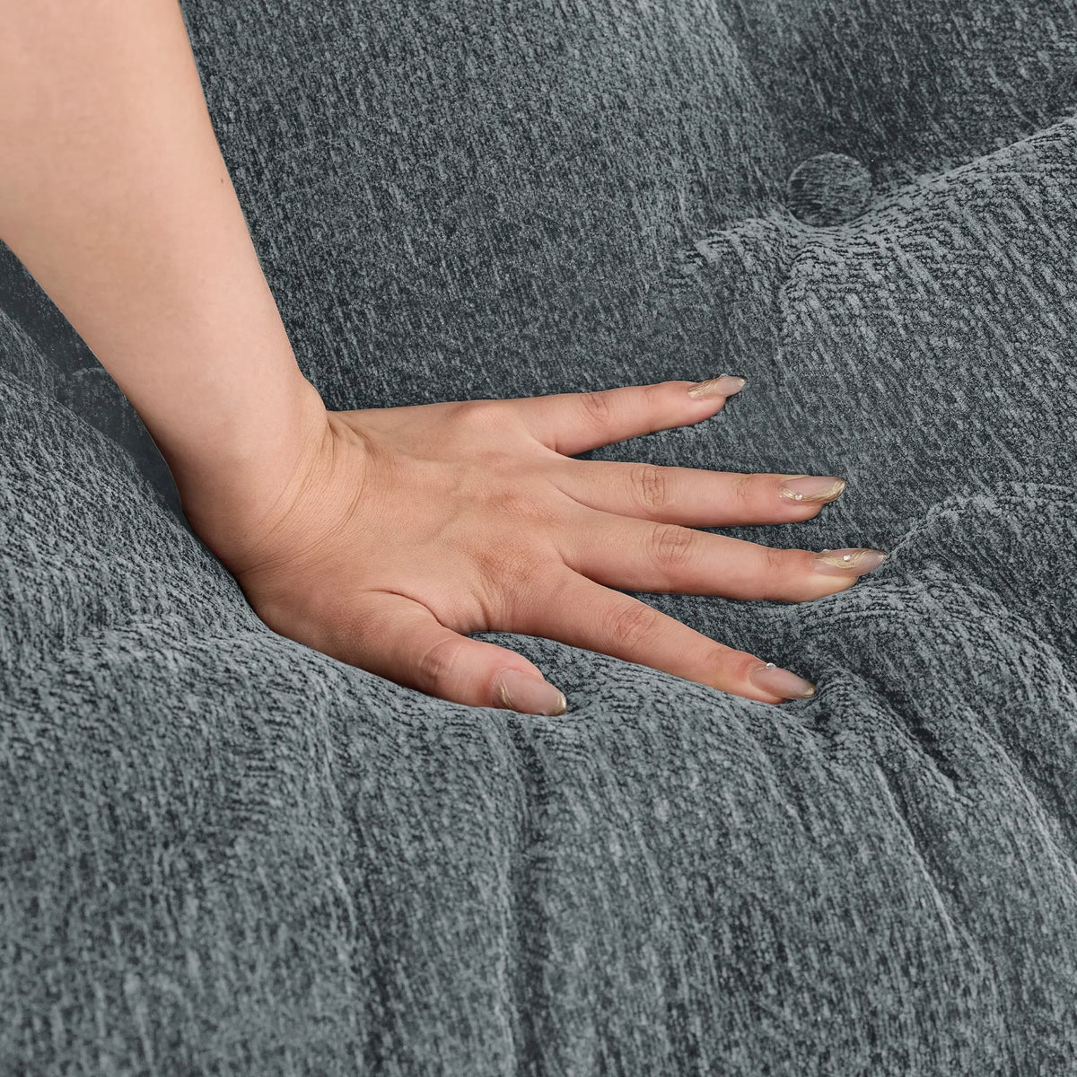 Close-up of a hand pressing the Korser grey fabric sofa cushion, demonstrating its softness and resilience.