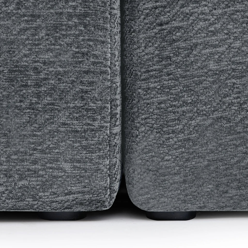 Close-up of the connection point between two Korser grey fabric sofa modules, showing the black support feet.