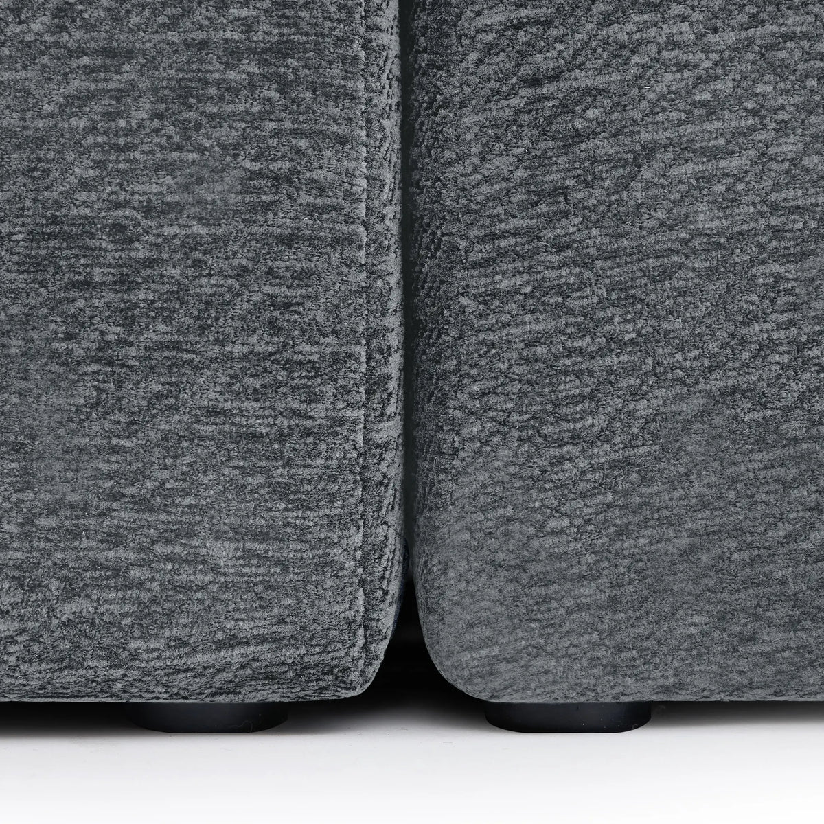 Close-up of the connection point between two Korser grey fabric sofa modules, showing the black support feet.